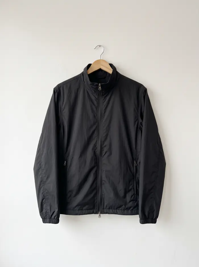 Campera de nylon negra colgada de una percha contra pared blanca