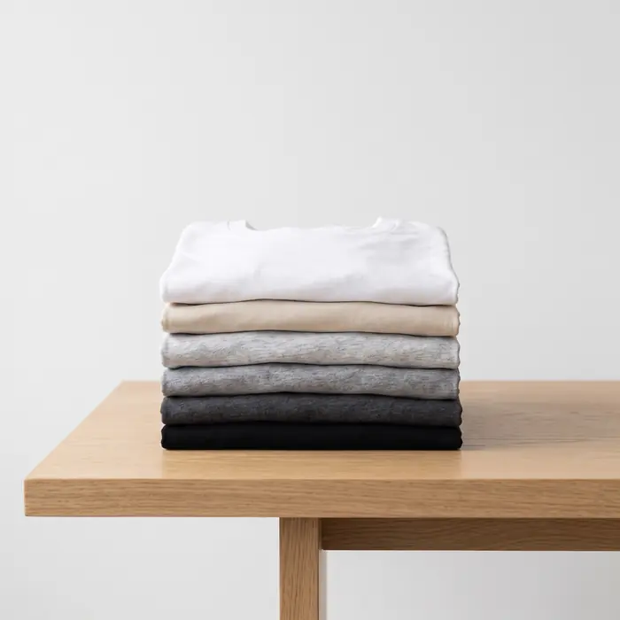 Pila de remeras dobladas en tonos blanco, crudo, gris y negro